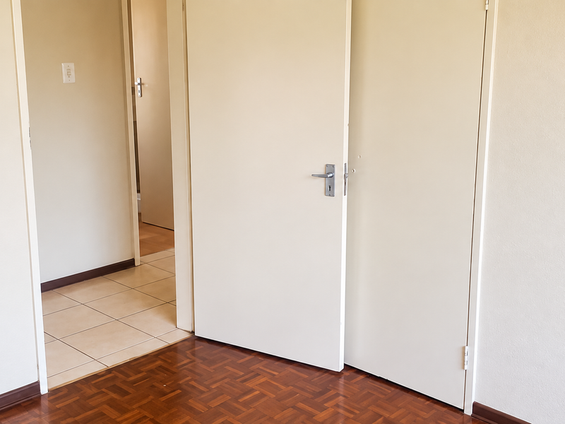 A clean, empty hallway featuring a transition between parquet wood flooring and ceramic floor tiles, with neutral walls and standard internal doors.