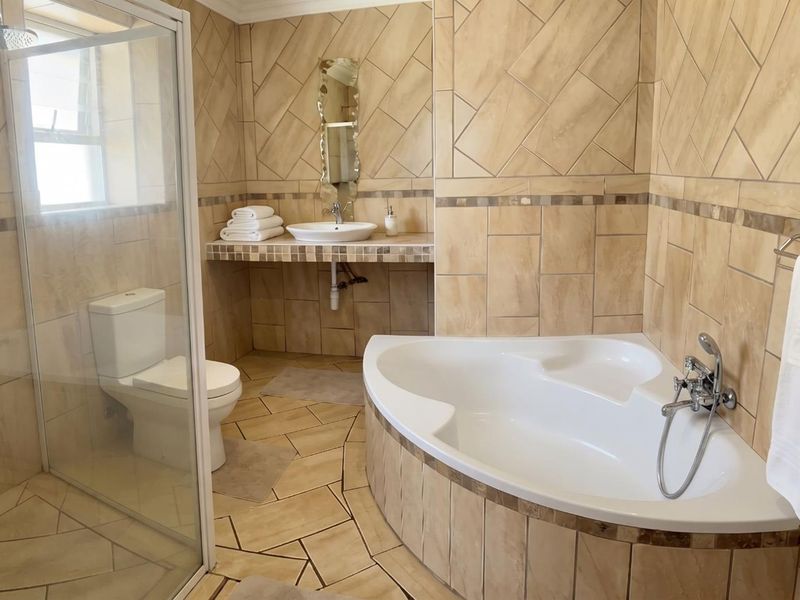 A spacious bathroom featuring a corner bathtub, a separate glass-enclosed shower with rainfall fixture, and a tiled vanity with a vessel sink.