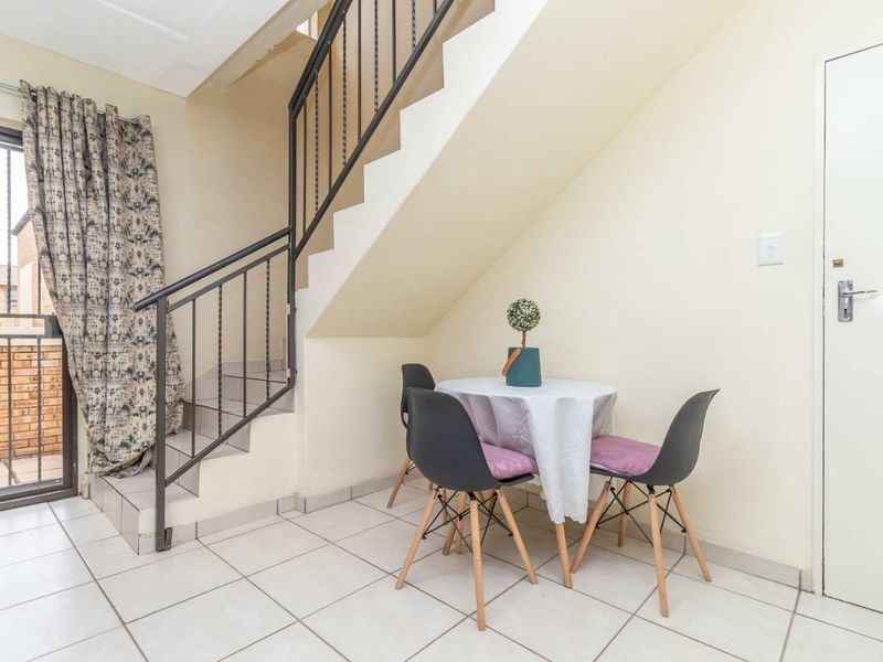 A bright living area featuring tiled flooring, a staircase with a metal balustrade, and a sliding door providing access to the exterior.