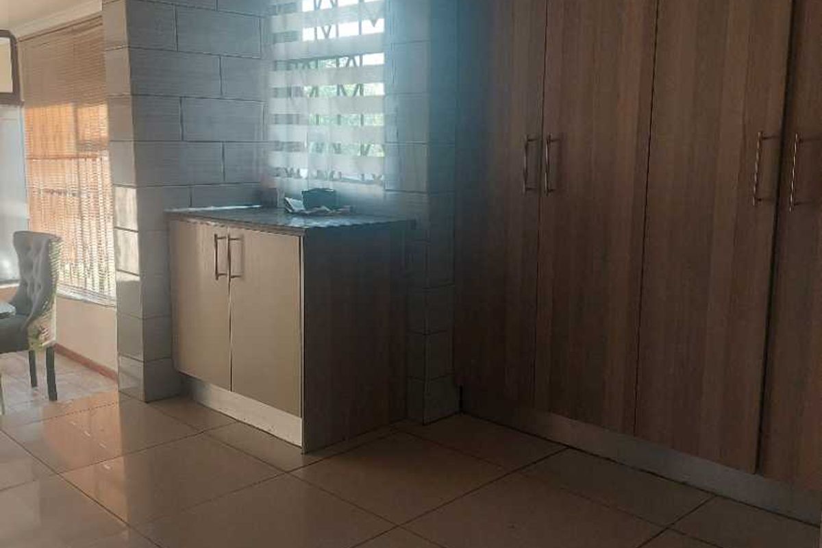 A spacious bedroom featuring modern tiled flooring, built-in wooden cupboards, and a distinctive stone-look feature wall with natural light.