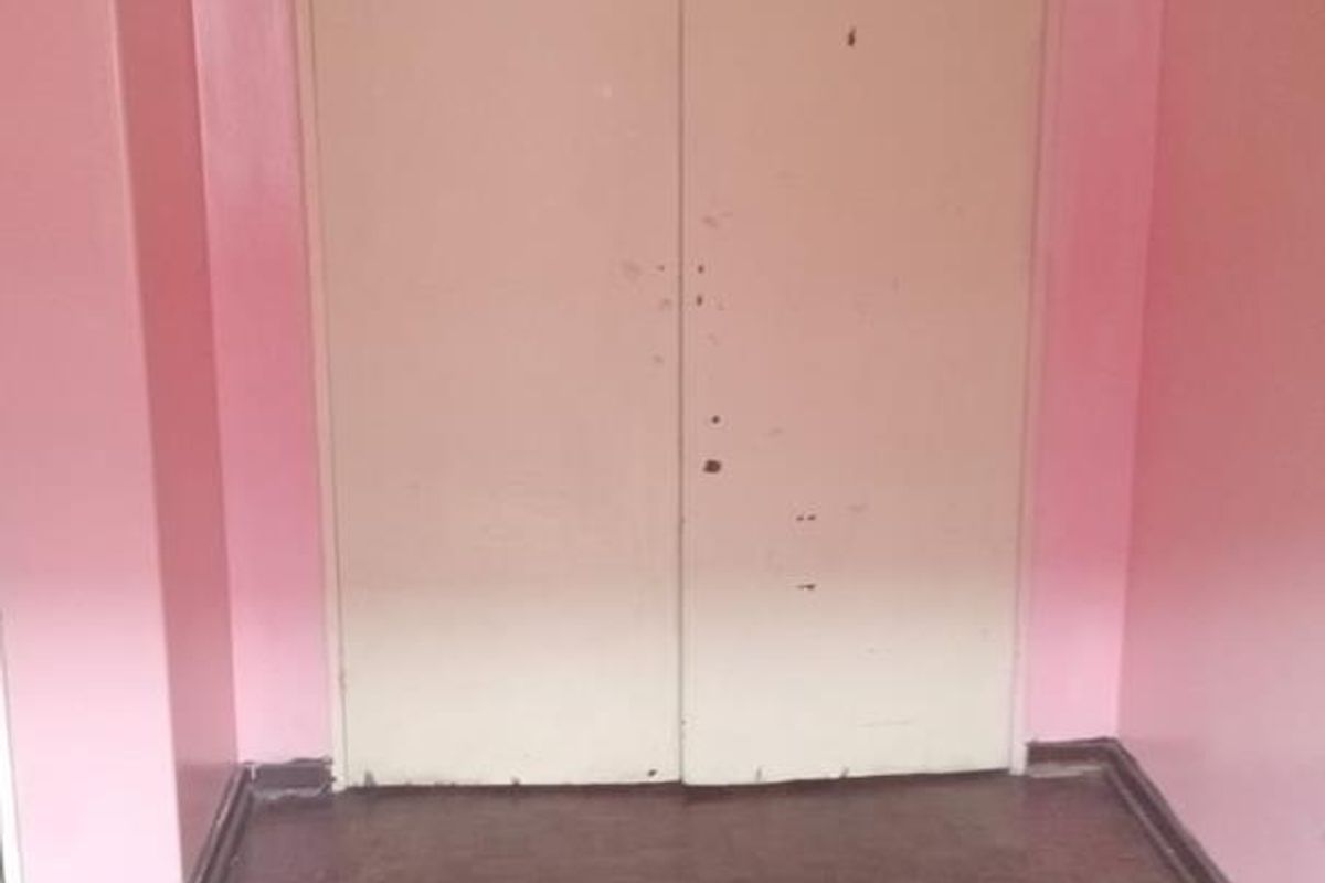 A bedroom featuring built-in cupboards with overhead storage, parquet flooring, and pink painted walls.