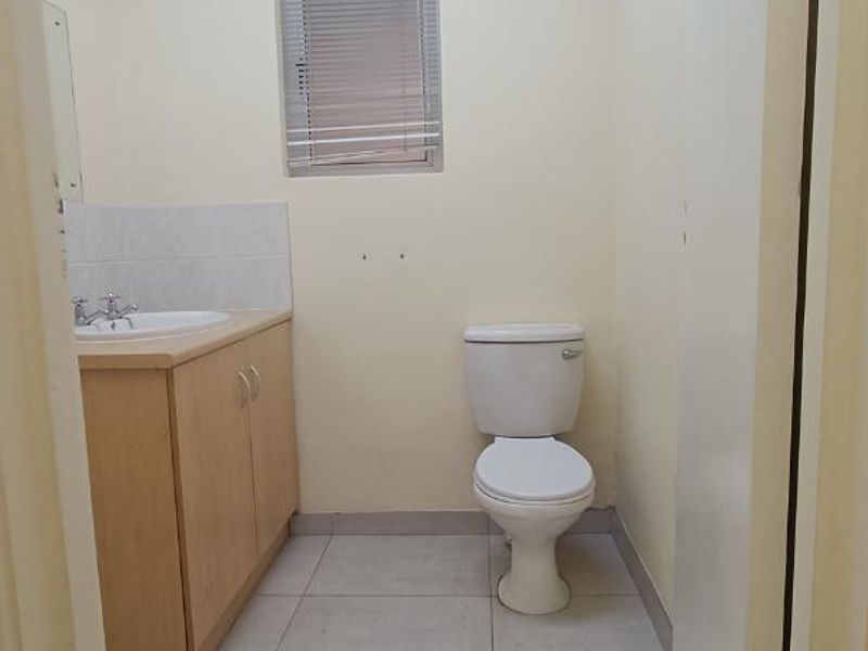 A functional, empty bathroom featuring a vanity cabinet with a basin, a standard toilet, tiled flooring, and a drop ceiling.