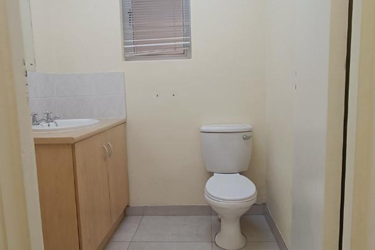 A functional, empty bathroom featuring a vanity cabinet with a basin, a standard toilet, tiled flooring, and a drop ceiling.