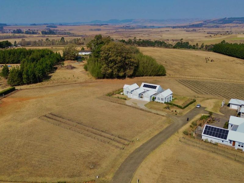 Aerial view of a residential property featuring multiple buildings with metal roofs, solar panel installations, and expansive surrounding rural land.