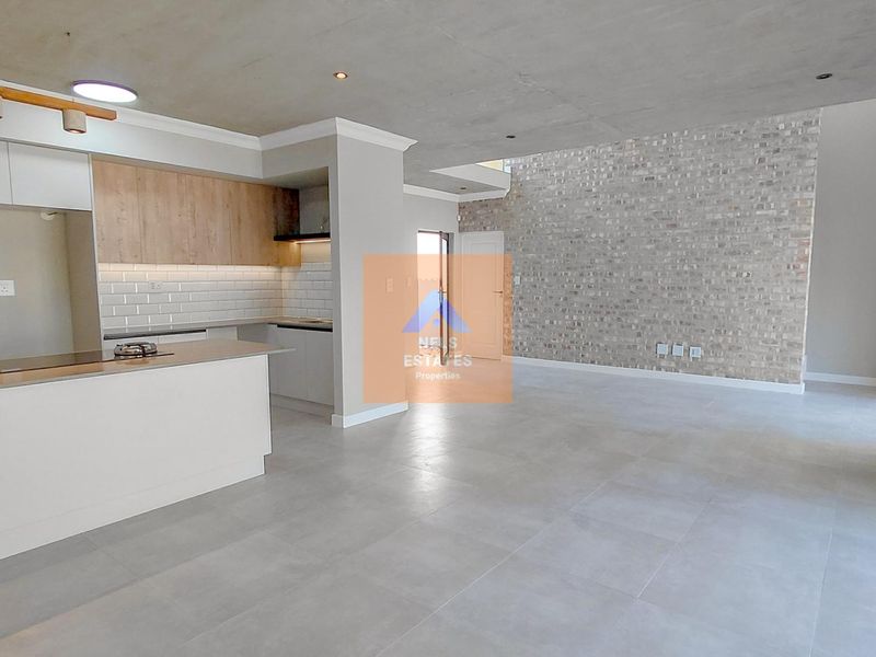 Modern open-plan living area featuring a contemporary kitchen with built-in cabinetry, stone countertops, and a striking exposed brick feature wall.