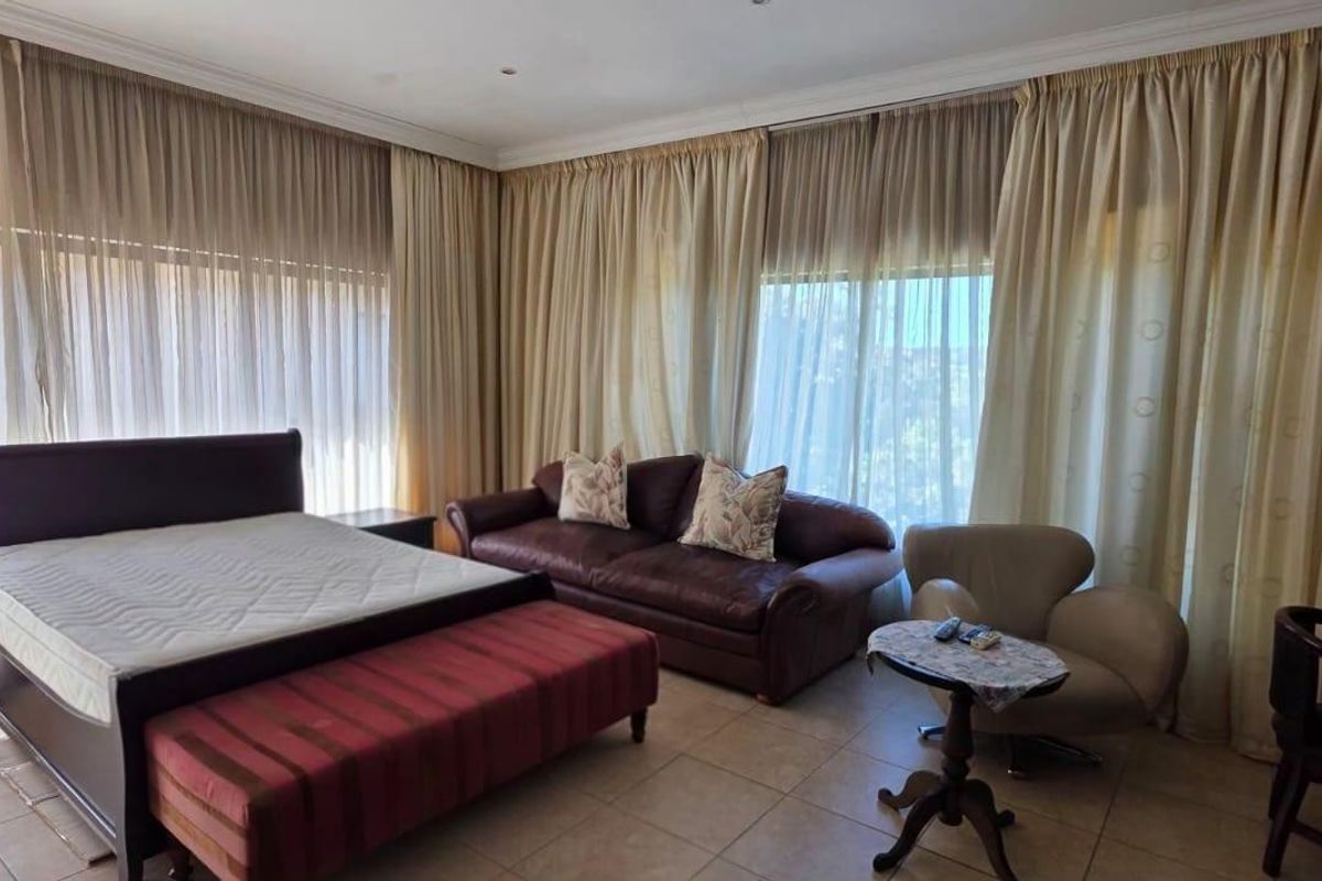 Spacious bedroom featuring large floor-to-ceiling windows with full-length curtains and neutral tiled flooring.
