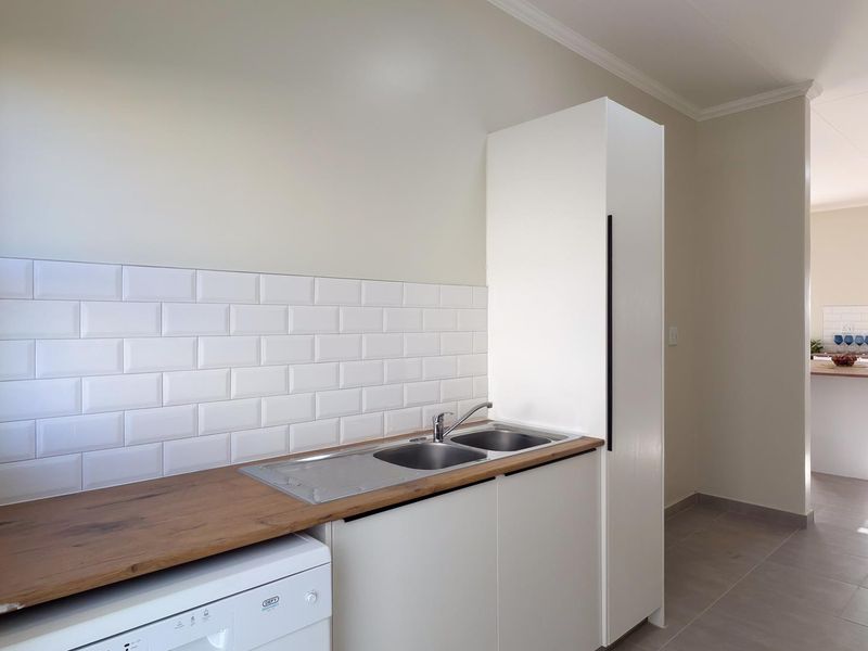 A clean and functional scullery area featuring a double bowl sink, timber-look countertop, white subway tile splashback, and ample built-in storage cabinetry.