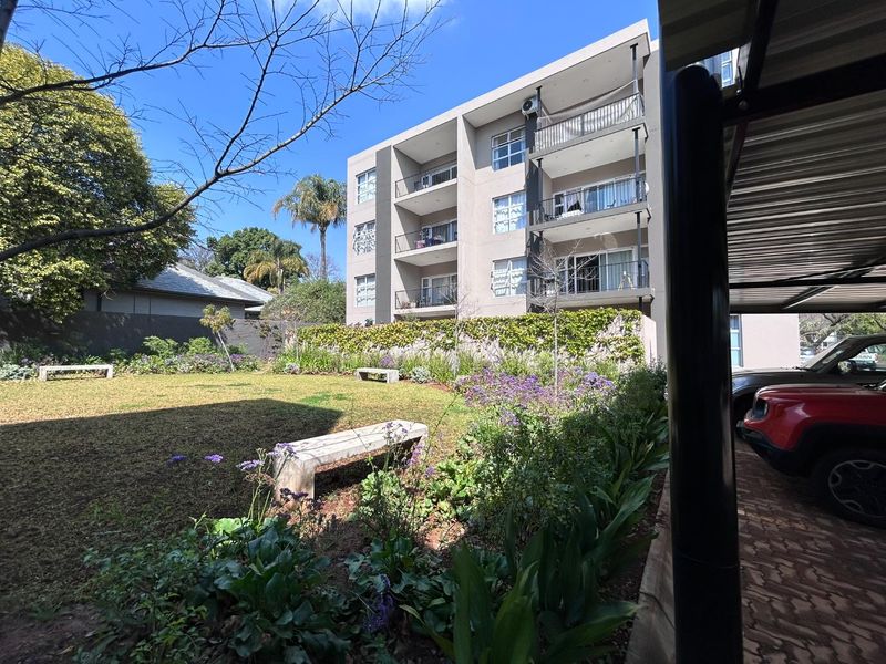 A view of the rear of the apartment complex featuring a well-maintained garden, stone benches, and covered parking facilities.