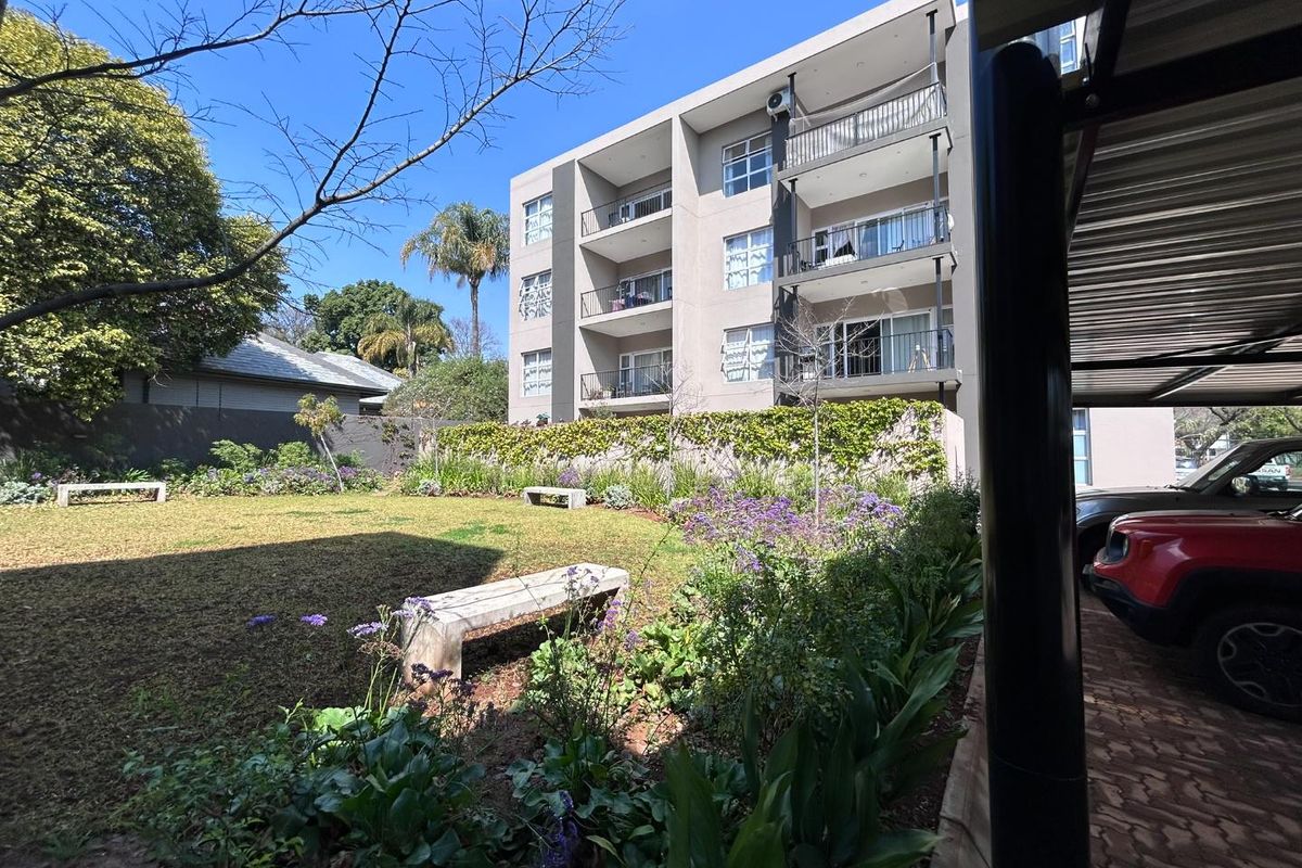 A view of the rear of the apartment complex featuring a well-maintained garden, stone benches, and covered parking facilities.