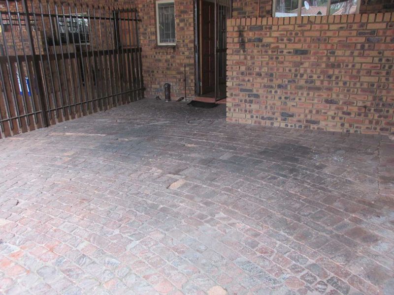 An exterior entrance area featuring brick paving and facebrick walls with a secure metal gate and entrance door.