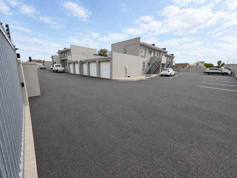 Exterior view of a townhouse complex featuring a paved driveway, multiple garage units, and external staircases providing access to upper levels.