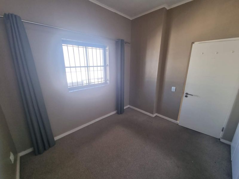 An empty bedroom featuring neutral wall paint, carpeted flooring, and a window fitted with security bars.