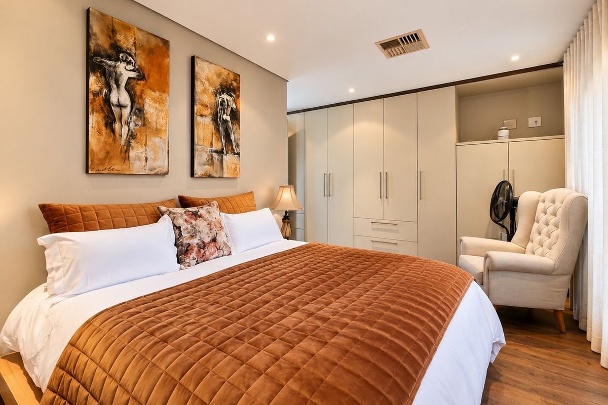 A well-maintained bedroom featuring extensive built-in cabinetry, recessed downlighting, ducted air conditioning, and warm-toned laminate flooring.