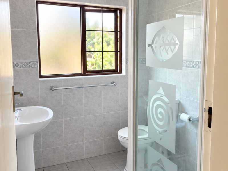 A functional bathroom featuring a pedestal basin, a shower enclosure with decorative glass, and a toilet, finished with neutral wall and floor tiles.