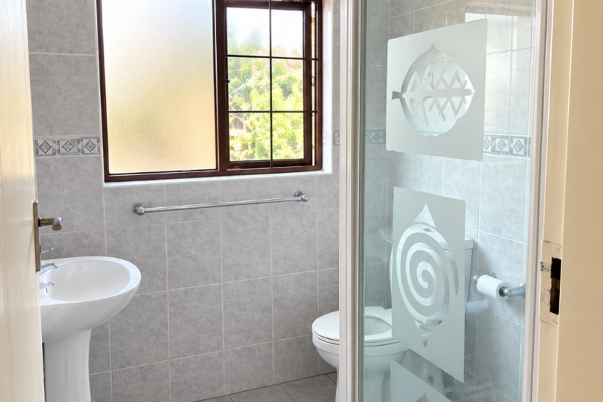A functional bathroom featuring a pedestal basin, a shower enclosure with decorative glass, and a toilet, finished with neutral wall and floor tiles.