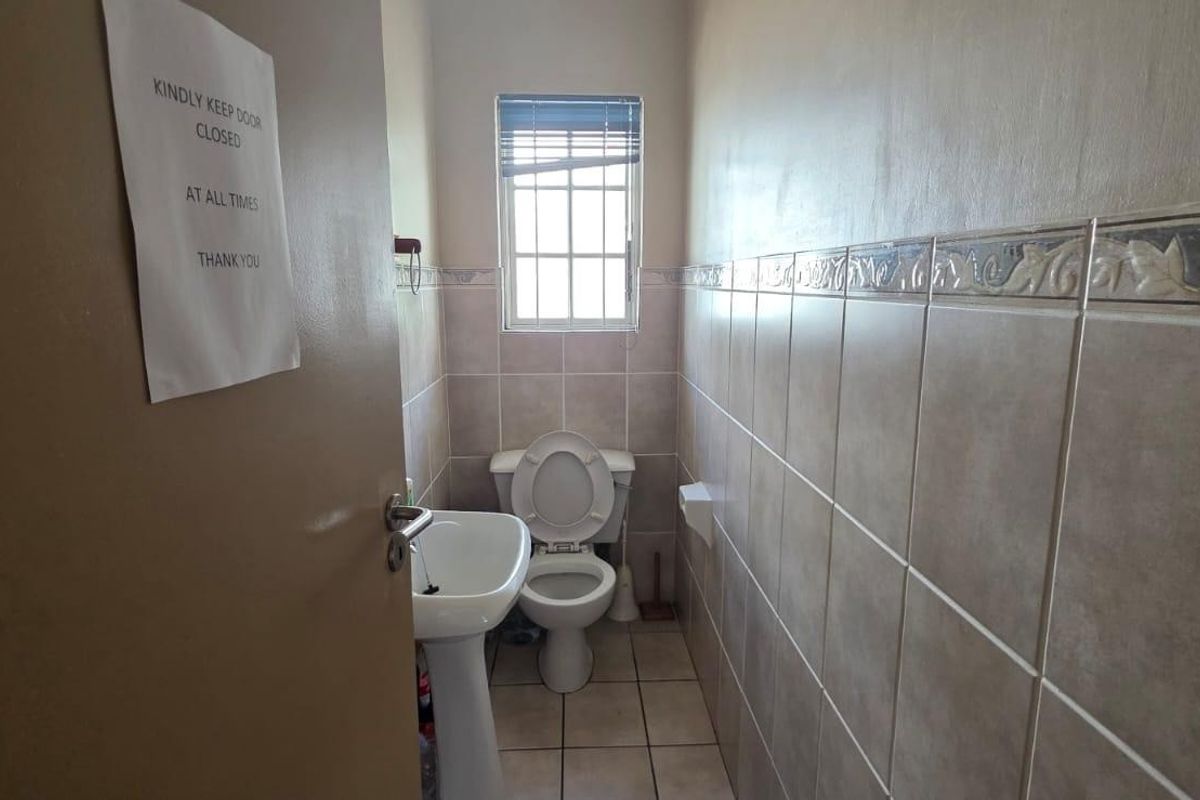 A functional, compact bathroom featuring a pedestal washbasin, toilet, and neutral ceramic wall and floor tiling.