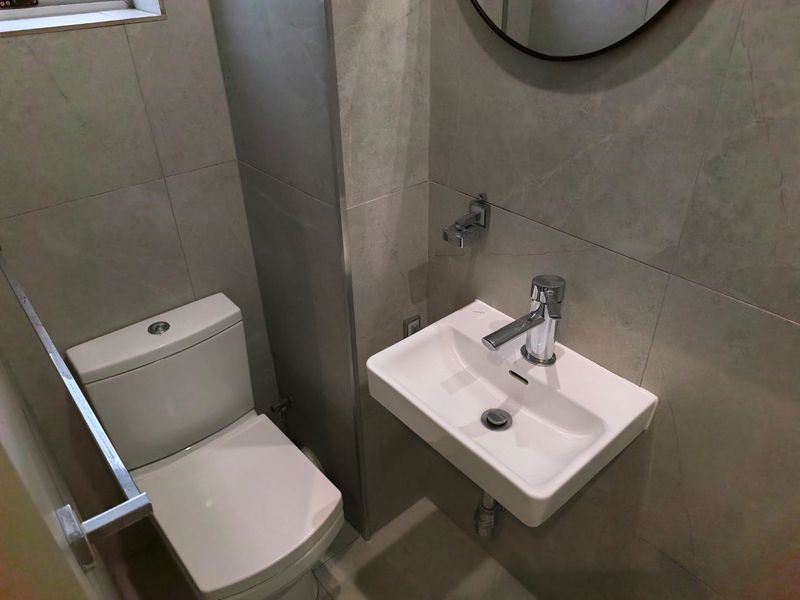 A modern, compact bathroom featuring a wall-mounted basin with chrome mixer and a dual-flush toilet, finished with neutral ceramic wall tiles.