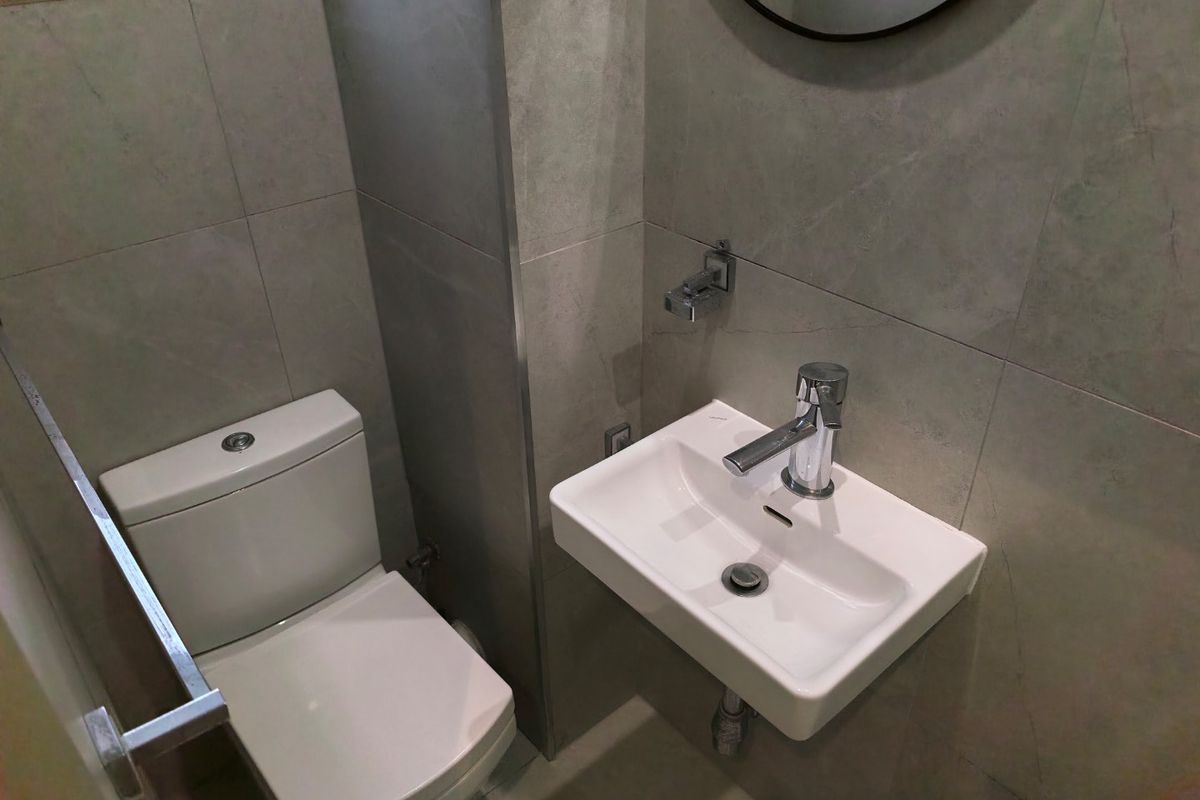 A modern, compact bathroom featuring a wall-mounted basin with chrome mixer and a dual-flush toilet, finished with neutral ceramic wall tiles.