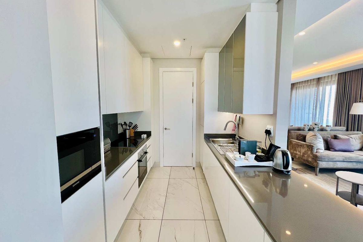 Modern galley-style kitchen featuring sleek white cabinetry, stone countertops, integrated Siemens oven and microwave, and polished marble-look floor tiles.