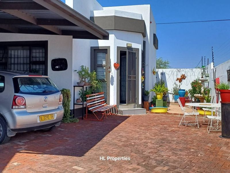 Front exterior view of the townhouse featuring a paved driveway, covered carport, and secure perimeter wall with electric fencing.