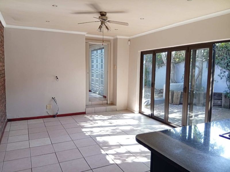 Open-plan living area featuring tiled floors, exposed brick accents, a ceiling fan, and large sliding glass doors providing access to the rear patio.