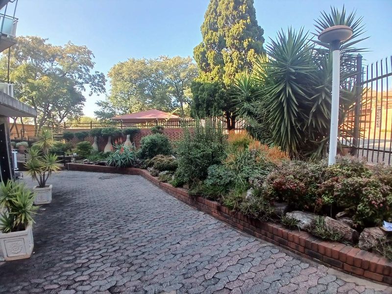 A well-maintained garden area featuring brick paving, a structured brick retaining wall, established landscaping, and secure perimeter fencing.
