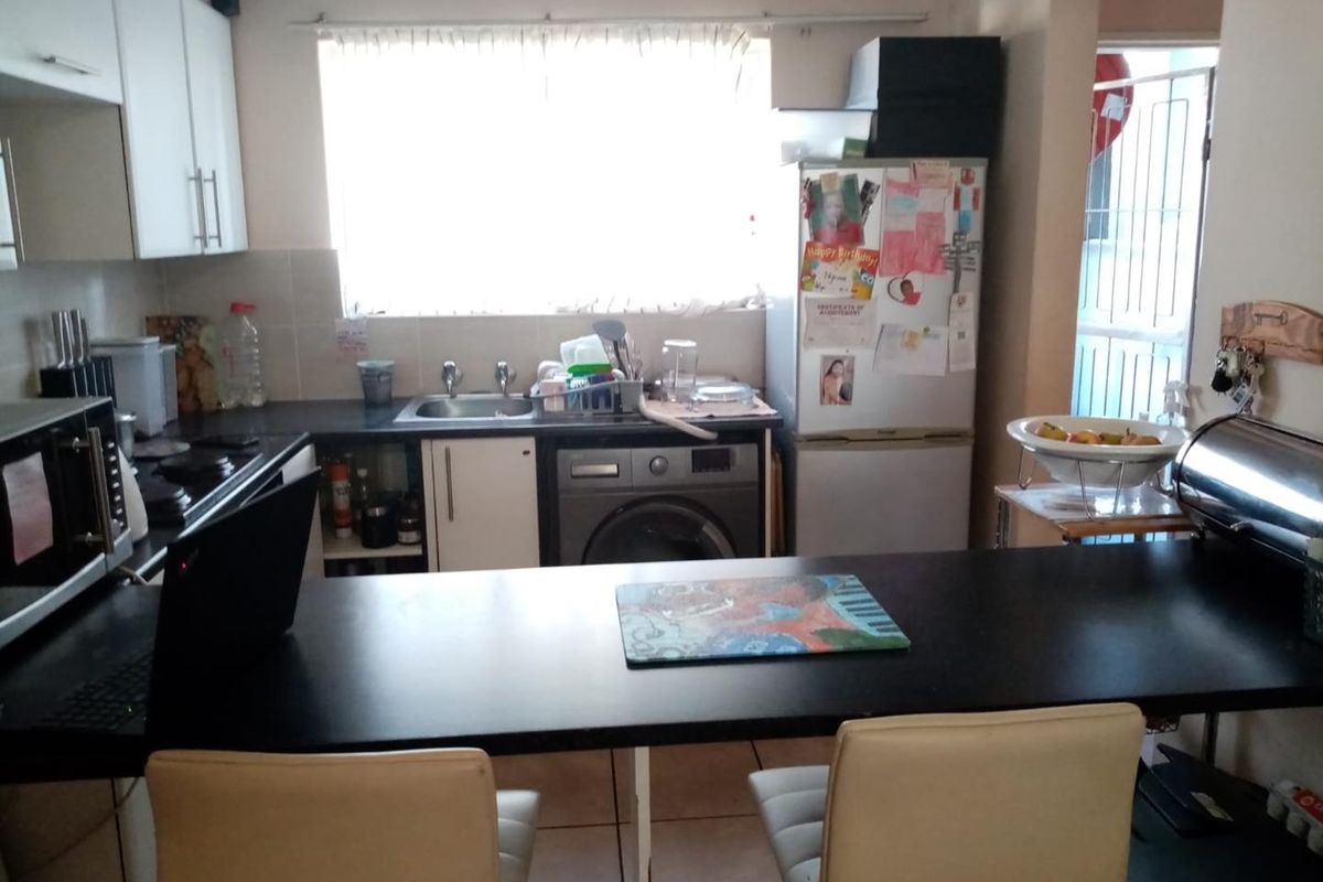 Functional kitchen featuring built-in cabinetry, dark laminate countertops, a stainless steel sink, and an integrated washing machine with a breakfast bar area.