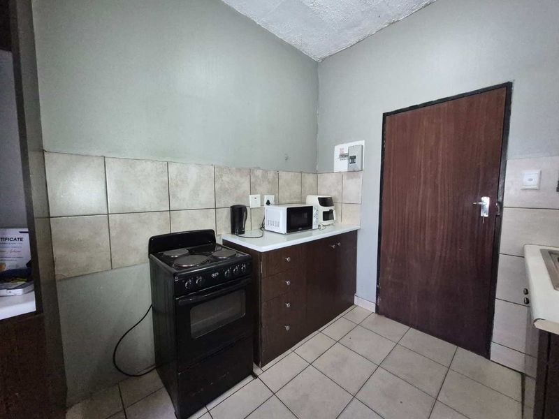 A compact kitchen area featuring tiled flooring, a tiled backsplash, built-in cabinetry, and a freestanding stove.