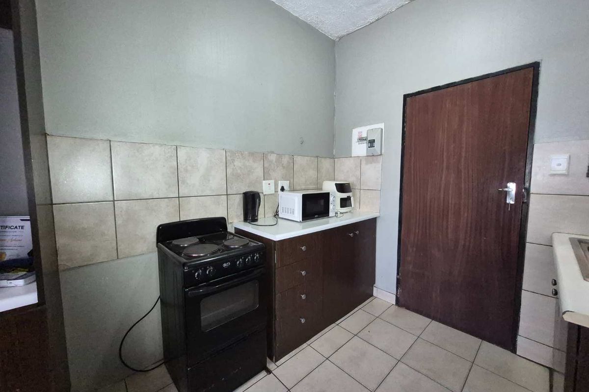 A compact kitchen area featuring tiled flooring, a tiled backsplash, built-in cabinetry, and a freestanding stove.
