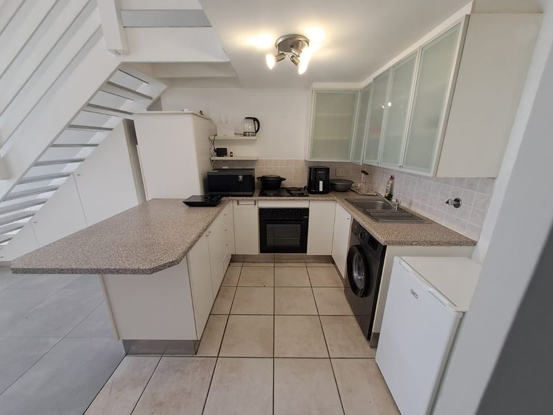 Compact kitchen featuring white cabinetry, laminate countertops, integrated oven and hob, and tiled flooring, conveniently located beneath a staircase.