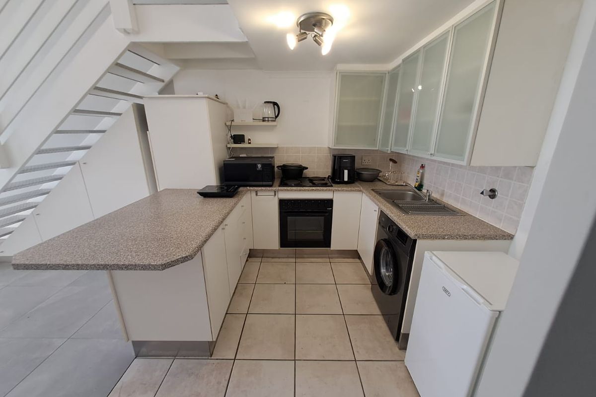 Compact kitchen featuring white cabinetry, laminate countertops, integrated oven and hob, and tiled flooring, conveniently located beneath a staircase.