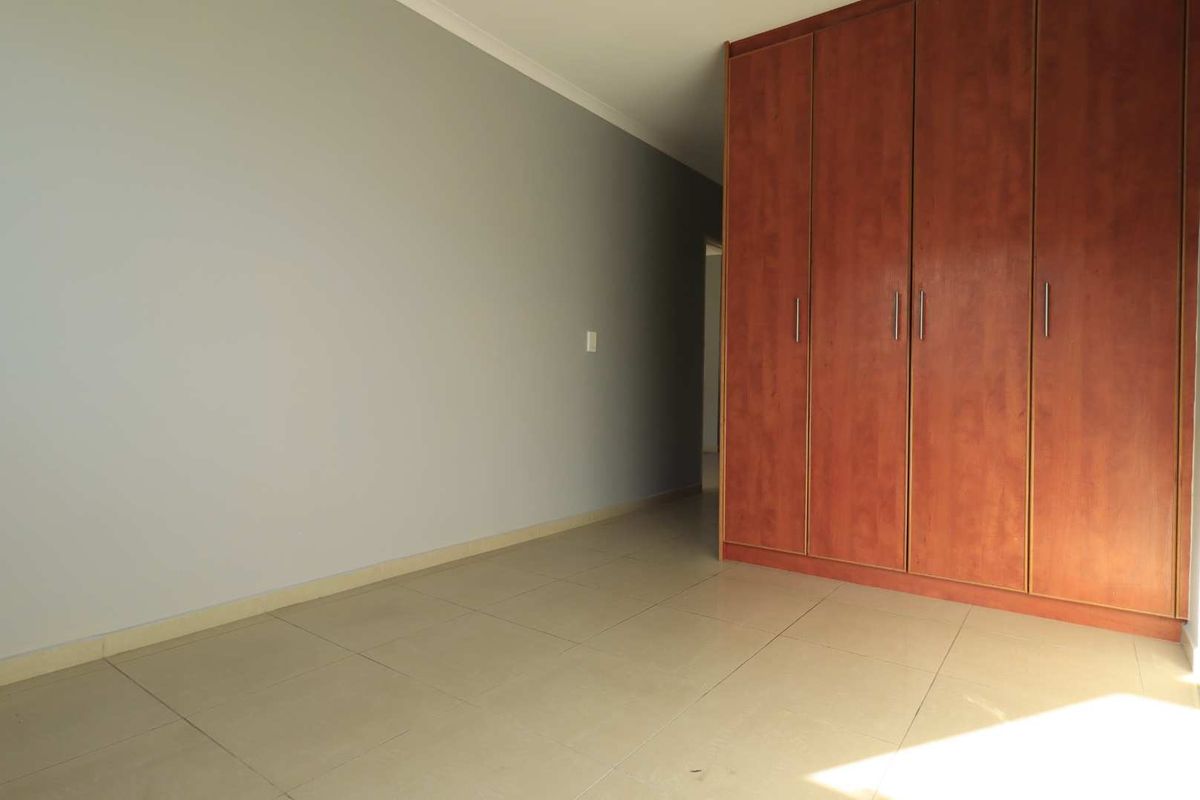 A bright, empty bedroom featuring neutral wall paint, tiled flooring, and built-in wooden cabinetry for storage.