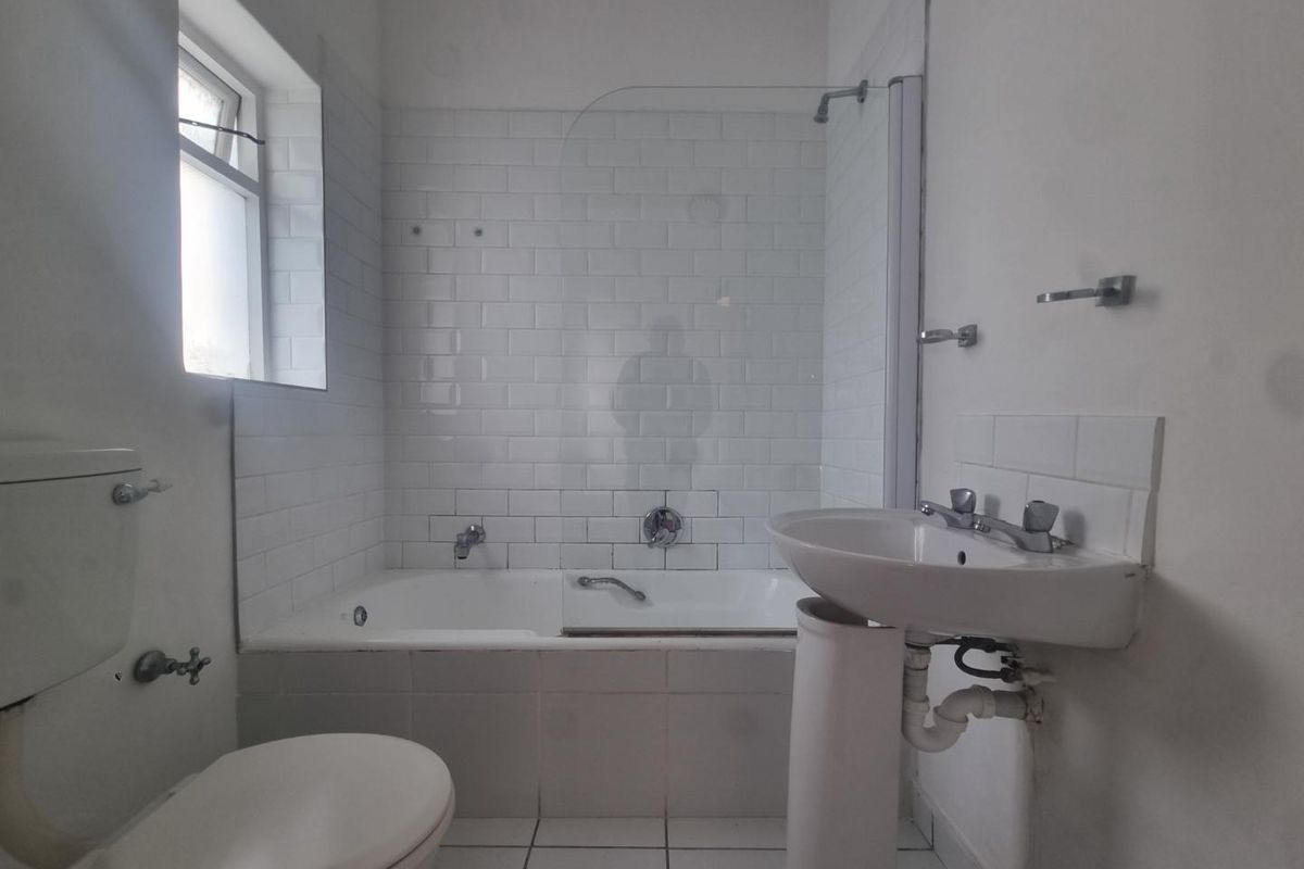A functional bathroom featuring a white pedestal basin, toilet, and a bathtub with subway tile surround and a glass shower screen.