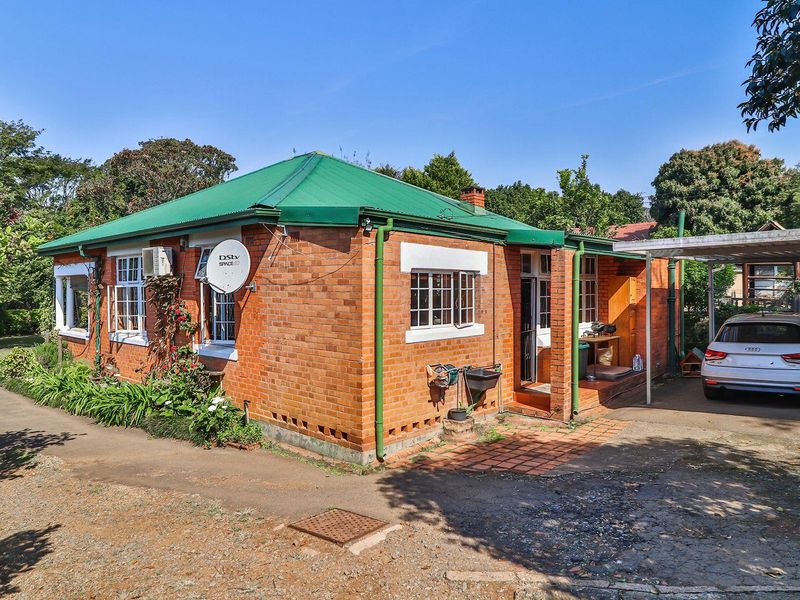 Rear view of a traditional brick house featuring a green metal roof, a covered carport, and a paved driveway area.