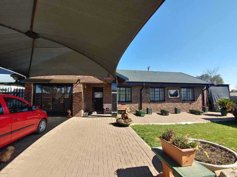 Front exterior view of a face brick house featuring a paved driveway, shade sail covering, and secure window bars.