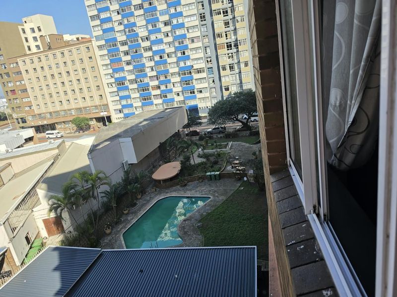Elevated view overlooking a communal swimming pool and garden area within an urban apartment complex setting.