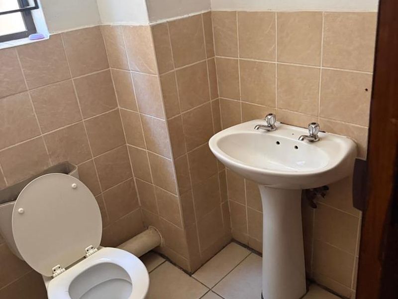 A functional bathroom featuring a pedestal basin, toilet, and neutral ceramic wall and floor tiling.