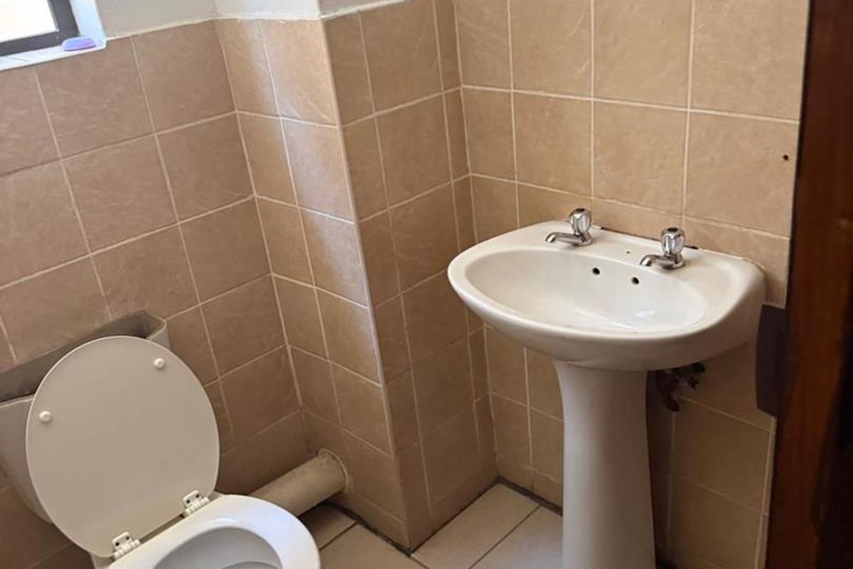 A functional bathroom featuring a pedestal basin, toilet, and neutral ceramic wall and floor tiling.