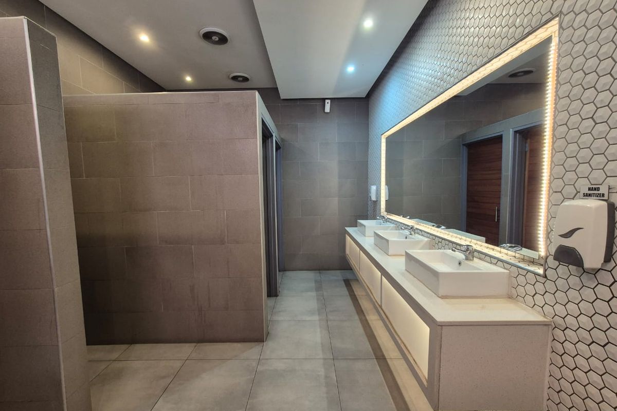 Modern commercial restroom featuring a floating vanity with dual vessel sinks, large backlit mirror, and contemporary tiled walls and flooring.
