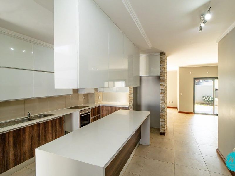 Modern open-plan kitchen featuring high-gloss cabinetry, stone countertops, a central island, and tiled flooring, flowing seamlessly into the adjacent living area.