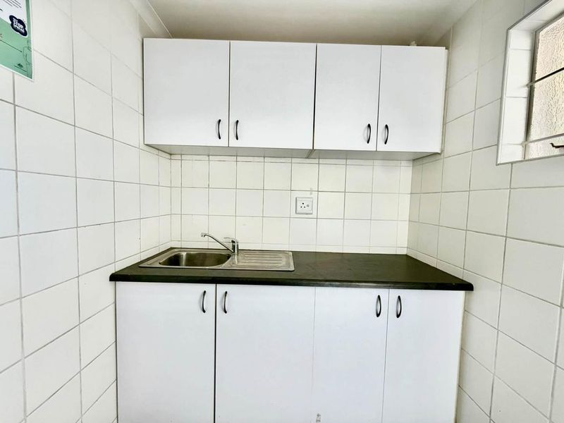 A functional scullery or kitchenette area featuring white built-in cabinetry, a stainless steel sink, and full-height wall tiling.
