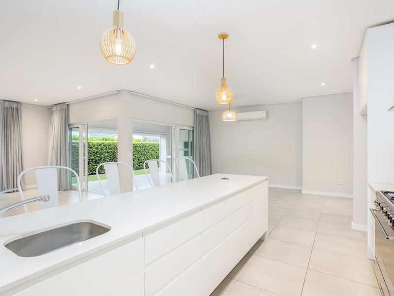 Modern open-plan kitchen and living area featuring a large island, sleek cabinetry, gas hob, and seamless access to the outdoor patio through sliding doors.