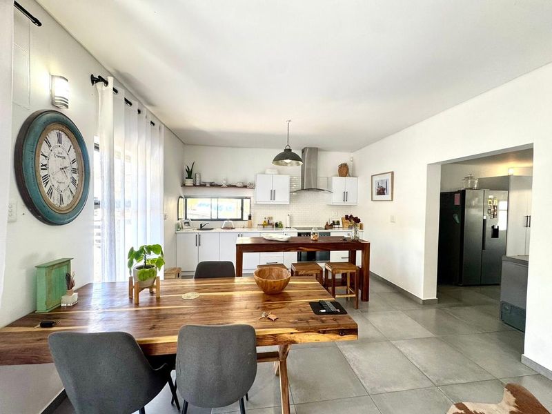 Open-plan kitchen and dining area featuring modern white cabinetry, subway tile backsplash, stainless steel extractor fan, and large format floor tiles.