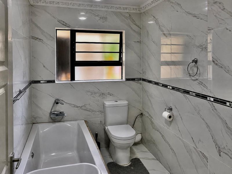 A modern, well-maintained bathroom featuring marble-effect wall tiles, a built-in bathtub, and a clean, contemporary layout.