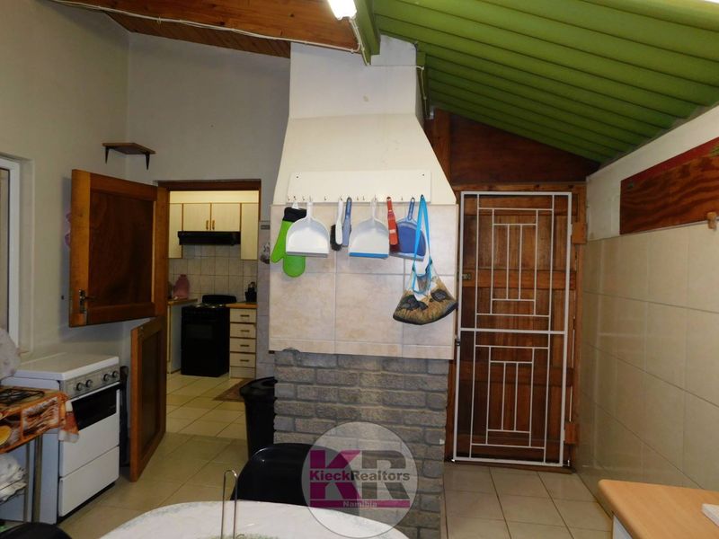 A functional kitchen area featuring exposed timber ceiling beams, tiled flooring, and a central brick chimney breast with access to an adjoining scullery space.
