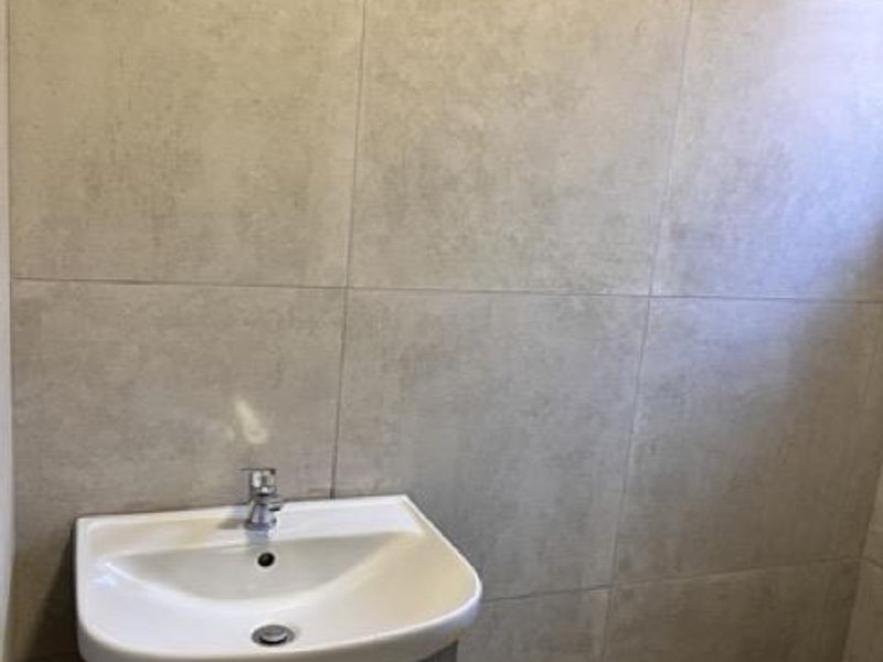 A clean, modern bathroom featuring large format wall tiles, a vanity cabinet with a basin, and a toilet.