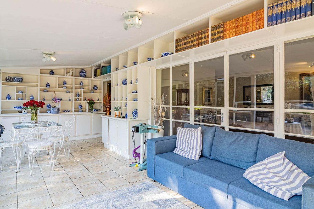 A bright sunroom featuring extensive built-in floor-to-ceiling shelving, tiled flooring, and large glass panel partitions connecting to the adjacent living space.