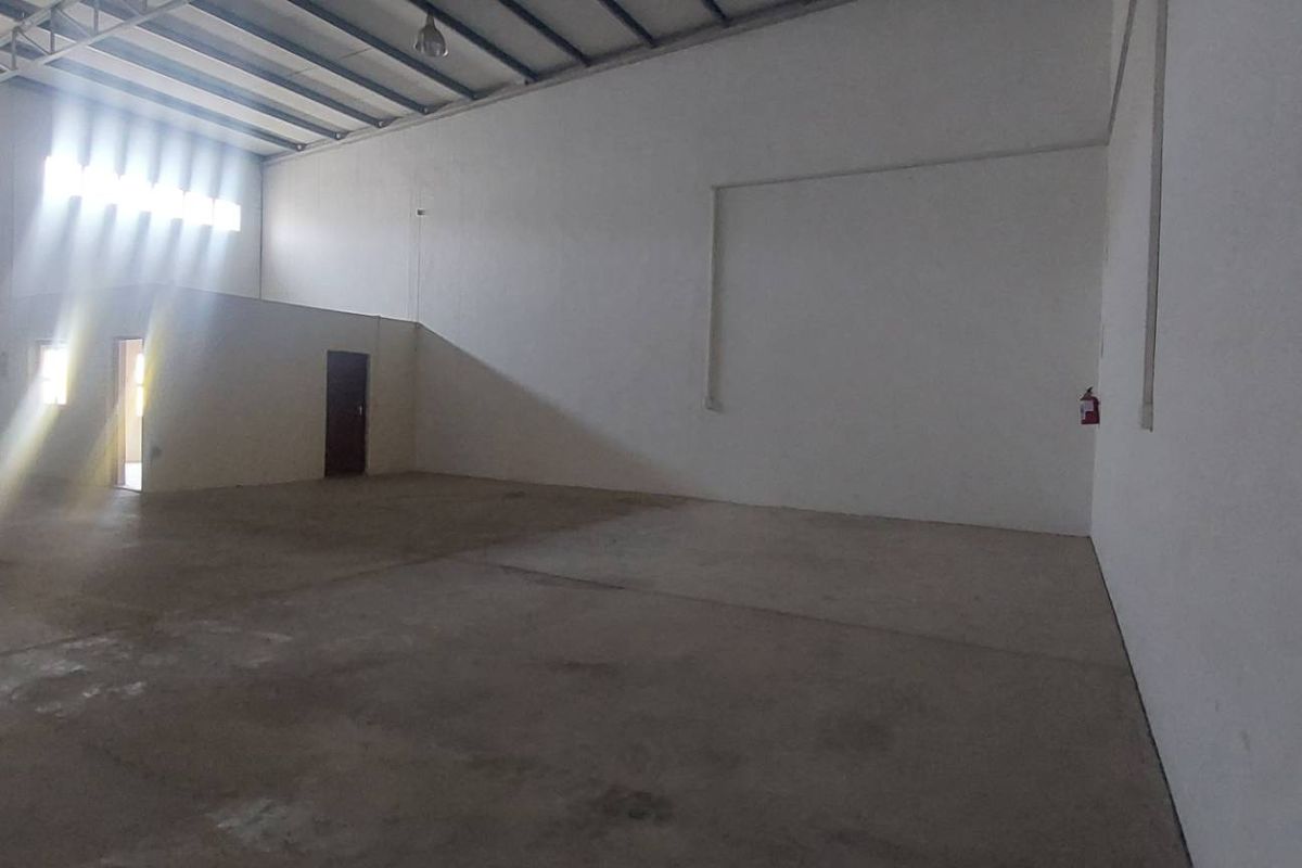 Spacious industrial warehouse unit featuring high ceilings with exposed steel trusses, concrete flooring, and a large roller shutter door for easy access.