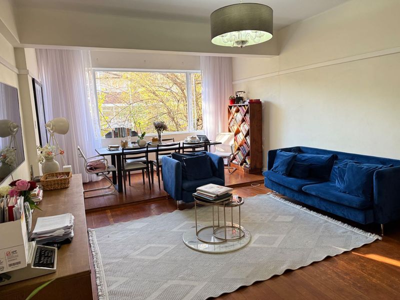 Spacious open-plan living and dining area featuring warm parquet flooring, a raised dining platform, and a large window providing ample natural light.