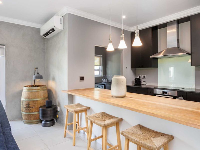 Modern open-plan kitchen featuring dark cabinetry, stone countertops, a breakfast bar, and integrated appliances, seamlessly flowing into the living area.